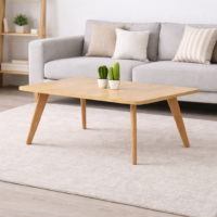 Table basse rectangulaire en bois clair avec pieds en bois naturel, intégrée dans un salon moderne avec canapé gris et tapis clair.