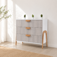 Commode scandinave gris clair et blanc à 3 tiroirs intégrée dans un décor minimaliste lumineux avec pieds en bois naturel.