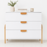 Commode blanche moderne à 3 tiroirs avec poignées et pieds en bois naturel dans un décor minimaliste.