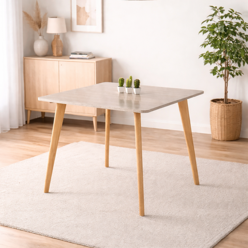 Table à manger carrée design scandinave avec plateau clair et pieds en bois naturel, intégrée dans un décor minimaliste sans chaises.