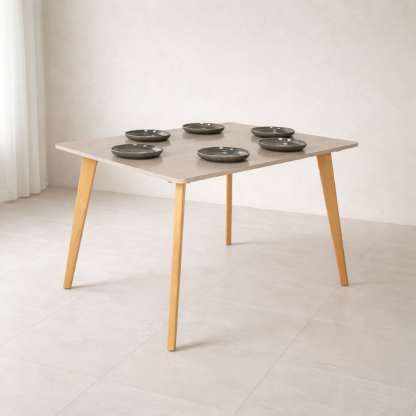 Table à manger carrée design scandinave en bois clair, mise en situation dans un décor naturel minimaliste sans chaises, avec vaisselle et éléments décoratifs.