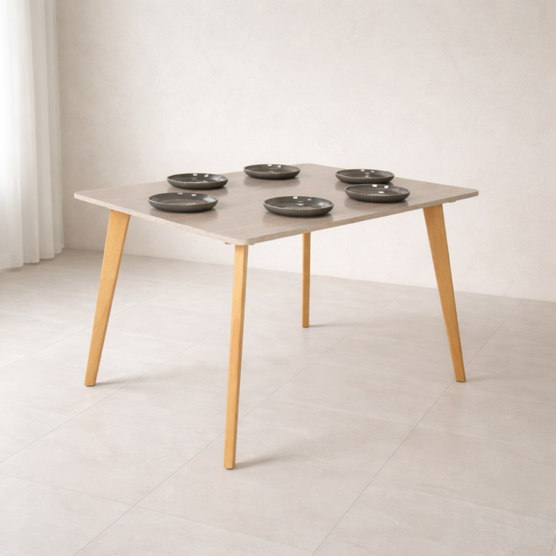 Table à manger carrée design scandinave en bois clair, mise en situation dans un décor naturel minimaliste sans chaises, avec vaisselle et éléments décoratifs.