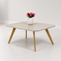 Table basse carrée en bois clair avec pieds en bois naturel, photographiée sur fond blanc avec vase décoratif.