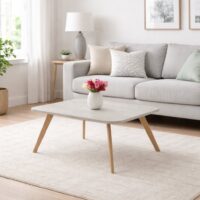 Table basse en bois clair avec pieds en bois naturel, intégrée dans un salon moderne avec canapé gris et tapis clair.