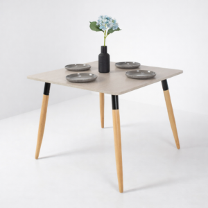 Table à manger moderne avec plateau clair et pieds en bois, décorée avec assiettes grises et vase floral, sur fond gris très clair – Tunisie