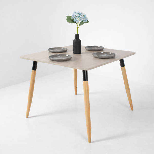 Table à manger moderne avec plateau clair et pieds en bois, décorée avec assiettes grises et vase floral, sur fond gris très clair – Tunisie