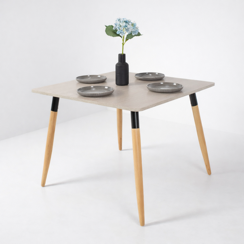 Table à manger moderne avec plateau clair et pieds en bois, décorée avec assiettes grises et vase floral, sur fond gris très clair – Tunisie