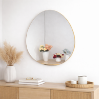 Miroir mural ovale avec cadre doré fin, accroché sur un mur blanc, reflétant un petit meuble en bois avec des vases décoratifs.