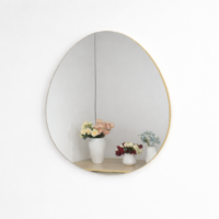 Miroir mural rond avec cadre doré fin, accroché sur un mur blanc, reflétant un petit meuble en bois avec des vases décoratifs.