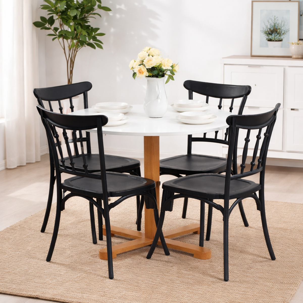 Table ronde blanche avec pied en bois et quatre chaises noires dans un décor lumineux avec tapis beige et plante verte