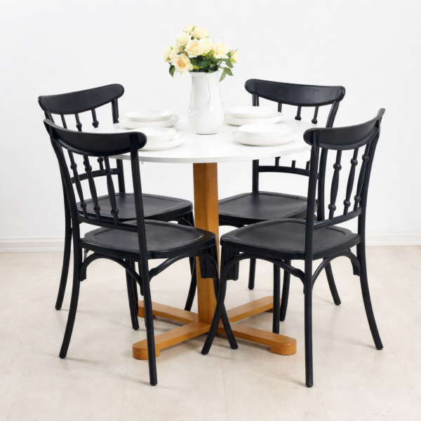 Table ronde blanche avec pied en bois et quatre chaises noires, décorée d’un vase de roses crème